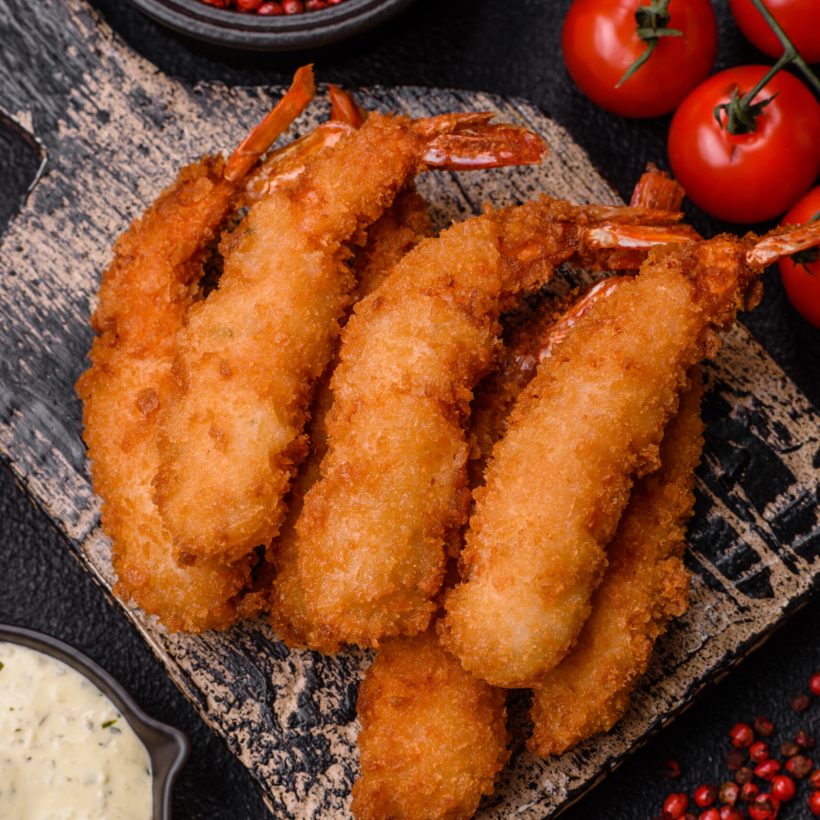 Hot crispy shrimp breaded with salt and spices with white sauce on a dark concrete background